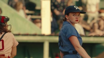 Movie still from “A League of Their Own” (2022), created by Abbi Jacobson – A woman in a baseball uniform is standing in the outfield; Medium shot, Over the shoulder angle