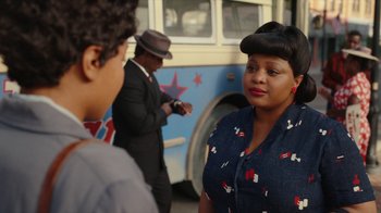 Movie still from “A League of Their Own” (2022), created by Abbi Jacobson – A woman standing in front of a bus with two men standing next to it; Close Up shot, Over the shoulder angle