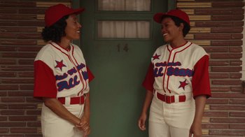 Movie still from “A League of Their Own” (2022), created by Abbi Jacobson – A couple of women standing next to each other in baseball uniforms; Medium shot, Overhead angle