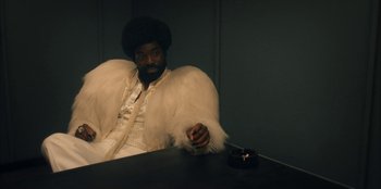 Movie still from “Black Mirror” (2011), created by Charlie Brooker – A man sitting at a table with a cigarette in his hand; Medium shot, Low angle