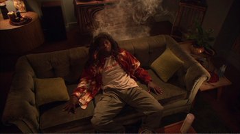 Movie still from “How High” (2001), directed by Jesse Dylan – A man laying on a couch smoking a cigarette; Wide shot, Overhead angle