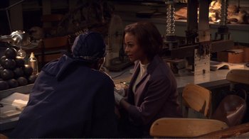Movie still from “How High” (2001), directed by Jesse Dylan – A woman sitting in front of another woman in front of a wooden table; Medium shot, High angle