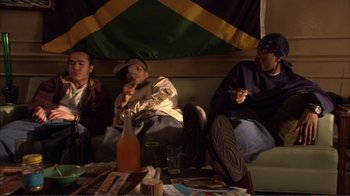 Movie still from “How High” (2001), directed by Jesse Dylan – A group of men sitting on a couch in front of a flag; Medium shot, High angle