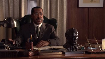 Movie still from “How High” (2001), directed by Jesse Dylan – A man sitting at a desk in front of a bust; Medium shot, High angle