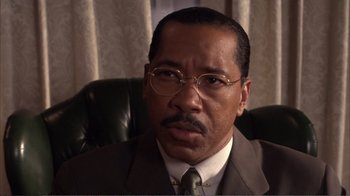 Movie still from “How High” (2001), directed by Jesse Dylan – A man in a suit and tie sitting in an office chair; Close Up shot, High angle