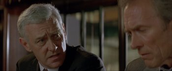 Movie still from “In the Line of Fire” (1993), directed by Wolfgang Petersen – An older man in a black suit looking at the camera; Close Up shot, Low angle