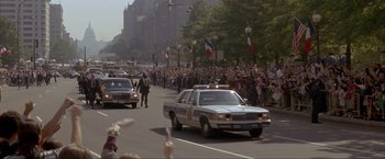 Movie still from “In the Line of Fire” (1993), directed by Wolfgang Petersen – A crowd of people gathered on a street with a police car; Extreme Wide shot, High angle