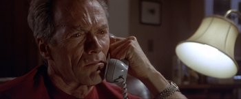 Movie still from “In the Line of Fire” (1993), directed by Wolfgang Petersen – An older man talking on a phone while sitting in a chair; Close Up shot, High angle