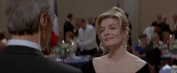 Movie still from “In the Line of Fire” (1993), directed by Wolfgang Petersen – A woman in a black dress is smiling at a party; Close Up shot, Over the shoulder angle