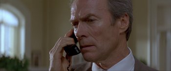 Movie still from “In the Line of Fire” (1993), directed by Wolfgang Petersen – An older man talking on a phone while wearing a suit and tie; Close Up shot, High angle