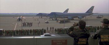 Movie still from “In the Line of Fire” (1993), directed by Wolfgang Petersen – A crowd of people standing on a tarmac near airplanes; Extreme Wide shot, Low angle