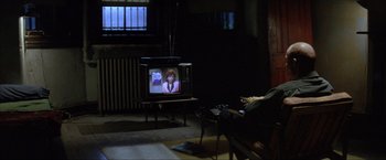 Movie still from “In the Line of Fire” (1993), directed by Wolfgang Petersen – A person sitting in a chair watching television; Wide shot, High angle