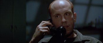 Movie still from “In the Line of Fire” (1993), directed by Wolfgang Petersen – A man talking on a phone while wearing a black shirt; Close Up shot, Low angle