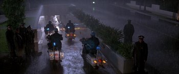 Movie still from “In the Line of Fire” (1993), directed by Wolfgang Petersen – A group of people riding motorcycles down a street in the rain; Wide shot, High angle