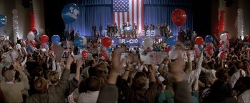 Movie still from “In the Line of Fire” (1993), directed by Wolfgang Petersen – A crowd of people in front of an american flag; Extreme Wide shot, High angle