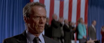 Movie still from “In the Line of Fire” (1993), directed by Wolfgang Petersen – An older man wearing a suit and tie in front of an american flag; Close Up shot, Low angle