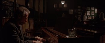 Movie still from “In the Line of Fire” (1993), directed by Wolfgang Petersen – A piano sitting in a dark room next to a glass of water; Medium shot, High angle