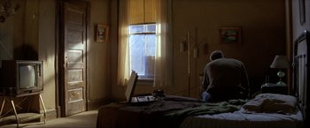 Movie still from “In the Line of Fire” (1993), directed by Wolfgang Petersen – A person sitting on a bed looking out a window; Wide shot, High angle