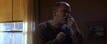 Movie still from “In the Line of Fire” (1993), directed by Wolfgang Petersen – A man in a brown sweater talking on a phone; Close Up shot, Low angle