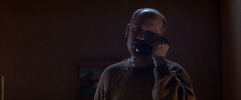 Movie still from “In the Line of Fire” (1993), directed by Wolfgang Petersen – A man talking on a phone in a dark room; Close Up shot, Low angle