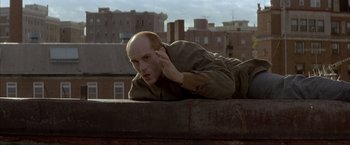 Movie still from “In the Line of Fire” (1993), directed by Wolfgang Petersen – A man laying on the side of a building on top of a building; Close Up shot, Low angle