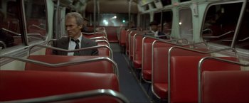 Movie still from “In the Line of Fire” (1993), directed by Wolfgang Petersen – A man in a suit and tie sitting on a bus; Wide shot, High angle