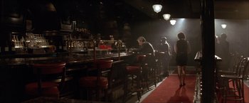 Movie still from “In the Line of Fire” (1993), directed by Wolfgang Petersen – A man sitting at a bar in front of a counter; Wide shot, High angle