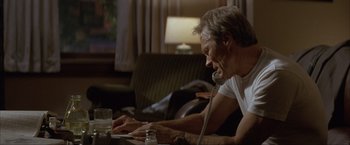 Movie still from “In the Line of Fire” (1993), directed by Wolfgang Petersen – A man sitting at a table talking on the phone; Medium shot, High angle
