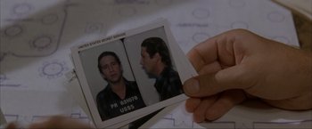 Movie still from “In the Line of Fire” (1993), directed by Wolfgang Petersen – A person holding a picture of a man in a prison uniform; Close Up shot, Overhead angle