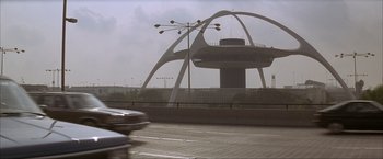 Movie still from “In the Line of Fire” (1993), directed by Wolfgang Petersen – A car driving down a street past a building with an arching structure; Extreme Wide shot, Low angle