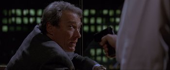 Movie still from “In the Line of Fire” (1993), directed by Wolfgang Petersen – A man in a suit and tie holding a gun in his hand; Close Up shot, Over the shoulder angle