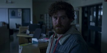 Movie still from “Black Summer” (2019), created by John Hyams – A man with curly hair and a beard is standing in a room; Close Up shot, Over the shoulder angle
