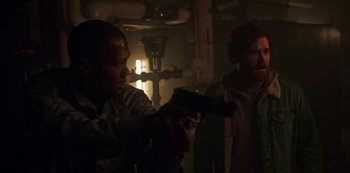 Movie still from “Black Summer” (2019), created by John Hyams – Two men are holding guns in a dimly - lit room; Medium shot, Over the shoulder angle