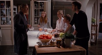 Movie still from “It's Complicated” (2009), directed by Nancy Meyers – A group of people standing around a table with food; Medium shot, Over the shoulder angle