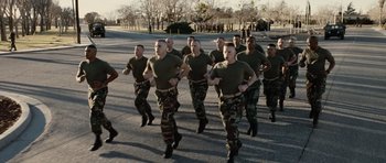 Movie still from “Jarhead” (2005), directed by Sam Mendes – A group of men in green shirts and camouflage pants running across a street; Wide shot, High angle
