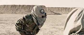 Movie still from “Jarhead” (2005), directed by Sam Mendes – A person wearing a gas mask in the middle of the desert; Medium shot, Over the shoulder angle