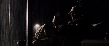 Movie still from “Jarhead” (2005), directed by Sam Mendes – A man sitting on a couch holding a cup of coffee; Medium shot, Low angle