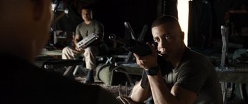 Movie still from “Jarhead” (2005), directed by Sam Mendes – A man holding a gun while sitting next to another man; Medium shot, Over the shoulder angle