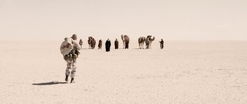 Movie still from “Jarhead” (2005), directed by Sam Mendes – A group of people standing in the desert with camels; Extreme Wide shot, Over the shoulder angle