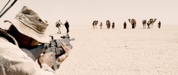 Movie still from “Jarhead” (2005), directed by Sam Mendes – A man is holding a rifle in the desert; Medium shot, Over the shoulder angle