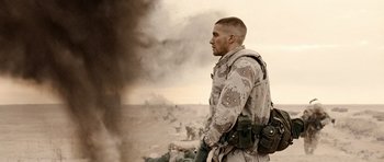 Movie still from “Jarhead” (2005), directed by Sam Mendes – A man in a military uniform standing in front of a smoke filled sky; Medium shot, Over the shoulder angle