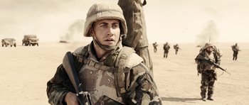 Movie still from “Jarhead” (2005), directed by Sam Mendes – A man in a military uniform holding a gun; Medium shot, Over the shoulder angle