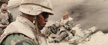 Movie still from “Jarhead” (2005), directed by Sam Mendes – Two men in fatigues sitting on the ground in the desert; Medium shot, Low angle
