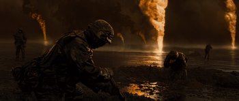 Movie still from “Jarhead” (2005), directed by Sam Mendes – A man in a black suit sitting on the ground near a body of water; Wide shot, High angle