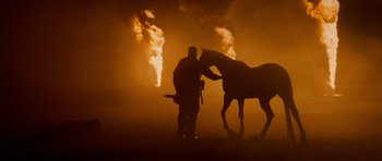 Movie still from “Jarhead” (2005), directed by Sam Mendes – A man standing next to a horse in a field; Wide shot, Low angle