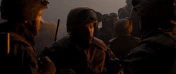 Movie still from “Jarhead” (2005), directed by Sam Mendes – A man wearing a helmet and goggles in the middle of a group of people; Close Up shot, Over the shoulder angle