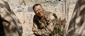 Movie still from “Jarhead” (2005), directed by Sam Mendes – A man in a military uniform sitting on the ground in front of a wall; Medium shot, Over the shoulder angle