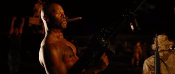 Movie still from “Jarhead” (2005), directed by Sam Mendes – A shirtless man holding a gun and smoking a cigar; Medium shot, Low angle