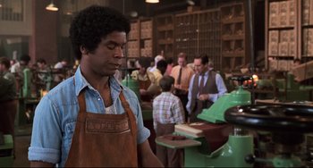 Movie still from “Jumanji” (1995), directed by Joe Johnston – A man in an apron standing next to a machine in a factory; Medium shot, Low angle