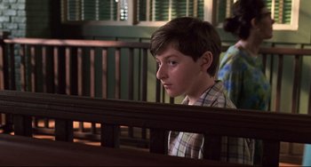 Movie still from “Jumanji” (1995), directed by Joe Johnston – A young boy sitting in a wooden bench; Medium shot, Over the shoulder angle